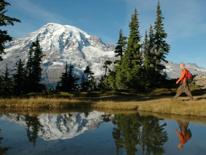 a young woman hikes by a small pond in front of mt. rainier, washington state